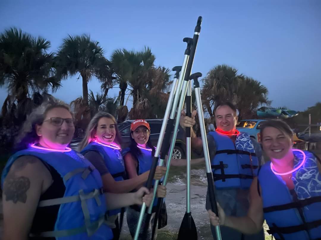 5 women holding up thier raft paddles prior to thier group rafting bioluminescence tour.